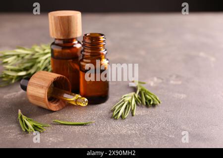 Essential oil in bottles, dropper and rosemary on grey table Stock Photo