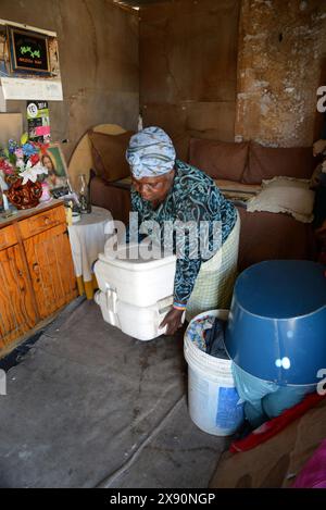 Grandmother Zondiwe Mhlaba moves her 'porta-potty' in her shack, Khayelitsha Stock Photo