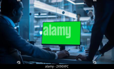 Two Developers Working on Computer with Green Screen Mock Up Display. Scientific Lab, Engineering Research Center with Specialists Working on Turbine Engine Development in the Background. Stock Photo