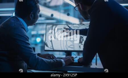 Two Turbine Engine Developers Working on Programming a Prototype Jet Engine on Desktop Computer. Young Team of International Industrial Science Specialists Developing a Turbine Motor in the Background Stock Photo
