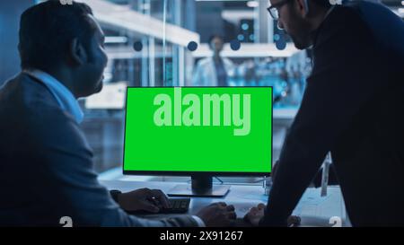 Two Developers Working on Computer with Green Screen Mock Up Display. Scientific Lab, Engineering Research Center with Specialists Working on Turbine Engine Development in the Background. Stock Photo
