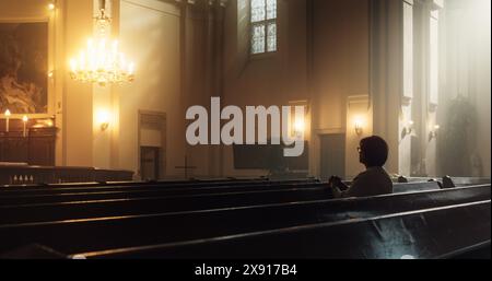 Christian Woman Sits Piously in Church, Praying, Seeks Guidance and Solace from Religious Faith and Spiritual Belief in God. Cinematic Camera Moving from Ceiling Painting of Jesus Christ to a Woman Stock Photo