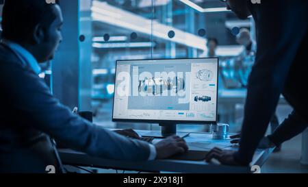 Two Turbine Engine Developers Working on Programming a Prototype Jet Engine on Desktop Computer. Young Team of International Industrial Science Specialists Developing a Turbine Motor in the Background Stock Photo