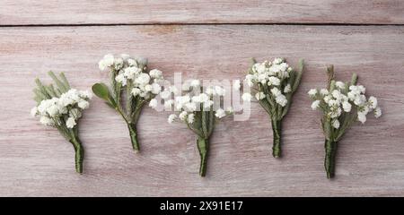 Many small stylish boutonnieres on light wooden table, flat lay Stock Photo