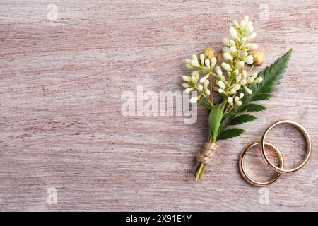 Small stylish boutonniere and rings on light wooden table, top view. Space for text Stock Photo