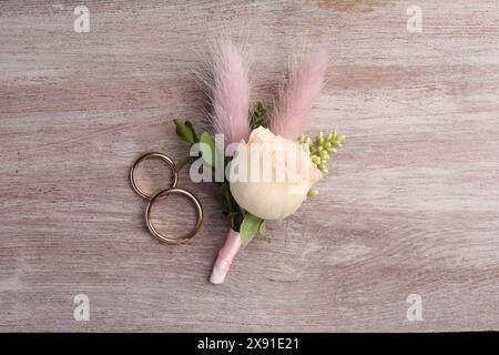 Small stylish boutonniere and rings on light wooden table, top view Stock Photo