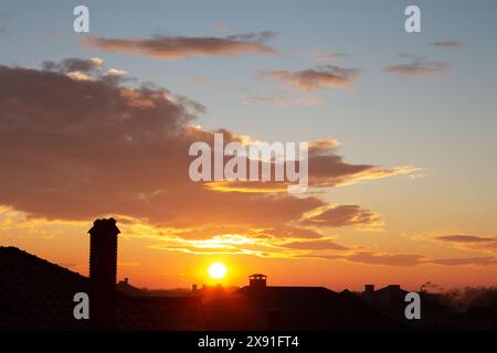 Beautiful sky at sunset. Bright orange clouds in the rays of the setting sun. Cumulus clouds, aerial background. Chimneys, tiled roof of house and bea Stock Photo