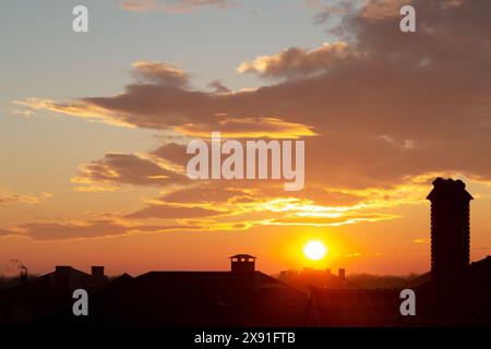 Beautiful sky at sunset. Bright orange clouds in the rays of the setting sun. Cumulus clouds, aerial background. Chimneys, tiled roof of house and bea Stock Photo