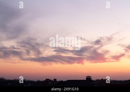 Beautiful sky at sunset. Bright clouds in the rays of the setting sun. Cumulus clouds, aerial background. Chimneys, tiled roof of house and beautiful Stock Photo