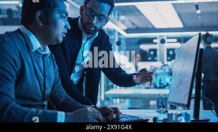 Two Turbine Engine Developers Working on Programming a Prototype Jet Engine on Desktop Computer. Young Team of International Industrial Science Specialists Developing a Turbine Motor in the Background Stock Photo