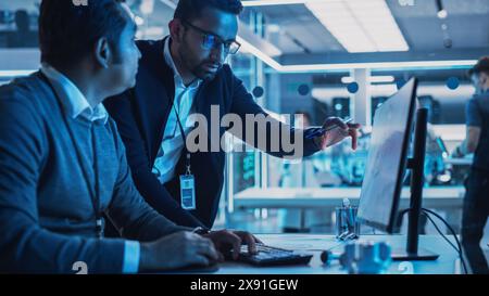 Two Developers Working on Computer with Green Screen Mock Up Display. Scientific Lab, Engineering Research Center with Specialists Working on Turbine Engine Development in the Background. Stock Photo