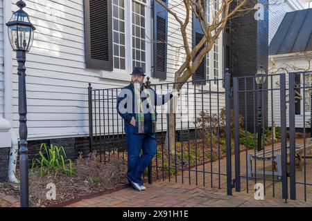 Wearing a hat and scarf a man stands in front of a garden courtyard gate in downtown Greenville, Tennessee, USA Stock Photo