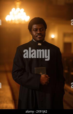 Portrait of a Young Black Priest Holding the Holy Bible in His Hand and Looking at the Camera. A Servant of God Helping Lost Souls Find the Path of Righteousness through Faith, Devoted to Christianity Stock Photo