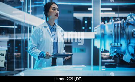 Young Asian Scientist Work on a New Type of Electric Turbine Engine, Standing and Using a Tablet Computer in Scientific Technology Laboratory. Stock Photo