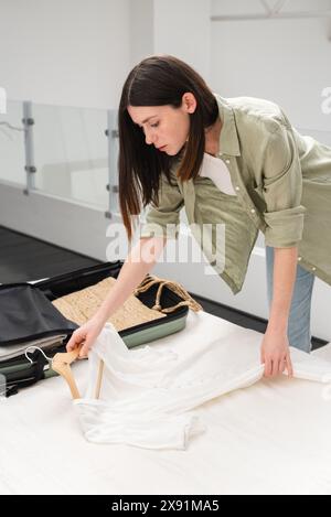 Young brunette woman packing suitcase for a solo traveling abroad. Summer vacation. Traveling overseas. Stock Photo