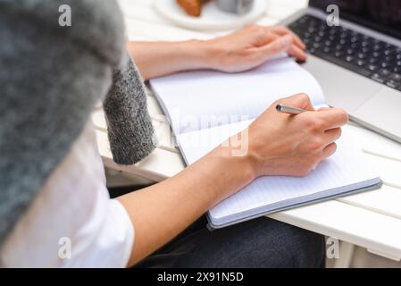 A woman takes notes in front of a laptop during an online business meeting outside. Stock Photo