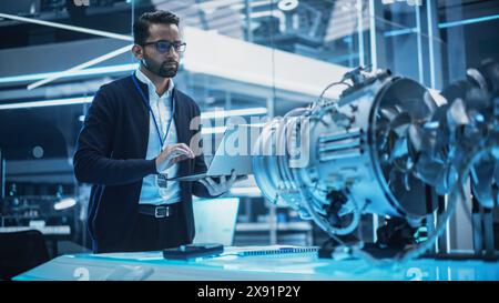 Young Industrial Engineer Working on a Futuristic Jet Engine, Standing with Laptop Computer in Scientific Technology Lab. Scientist Developing a New Electric Motor in a Research Facility. Stock Photo