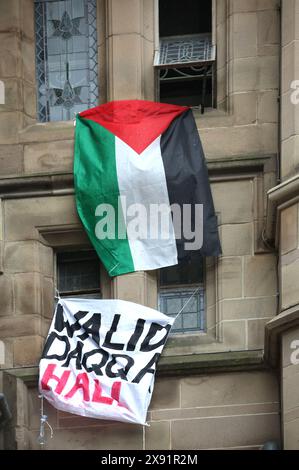 Students occupying and barricaded in Whitworth Hall renamed the building ‘Walid Daqqa Hall and a Palestinian flag flies from upper windows during a protest. Students and supporters occupy Brunswick Park now renamed by them as Dr Adnan Al-Bursh Park and Whitworth Hall at Manchester University. Protesters demand that the University Stop arming Israel and end their complicity in genocide. They insist that the University end their partnership with arms manufacturer BAE Systems, end their ties with Tel Aviv and Hebrew Universities in Israel and adopt a policy of ensuring all research is ethical and Stock Photo