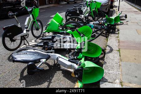 A jumble of green and black rental bikes lying scattered on the side of the road in disarray in London UK Stock Photo