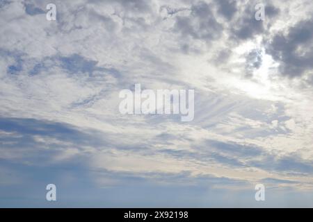 A cloudy sky with blue patches, the sun shining through the clouds from the top right Stock Photo