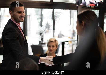 A diverse group of young business professionals handshake in a warmly lit cafe, suggesting teamwork and network expansion. Stock Photo