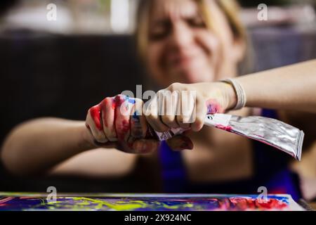 Close-up of a female artist squeezing multicolored paint from a tube onto a canvas, showcasing the creative process and artistic expression. Stock Photo