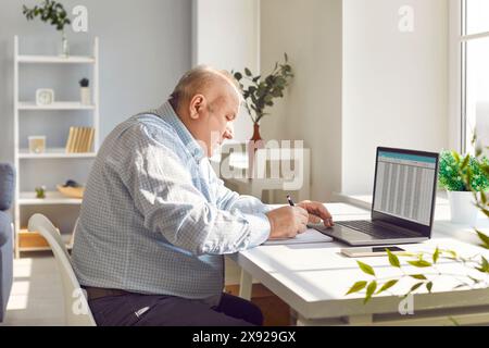 Old senior man working using laptop with chart sitting at the desk at home Stock Photo