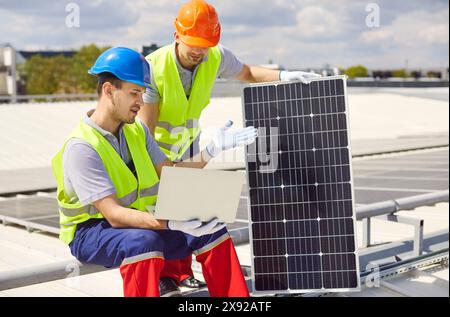 Repairmen Adjusting And Maintaining Solar Panels With Laptop On Roof Stock Photo