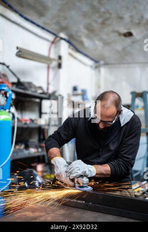 Using the flexible disc grinder on a metal bar: When the tool touches the surface, numerous orange sparks are projected. Vertical format. Concept of m Stock Photo