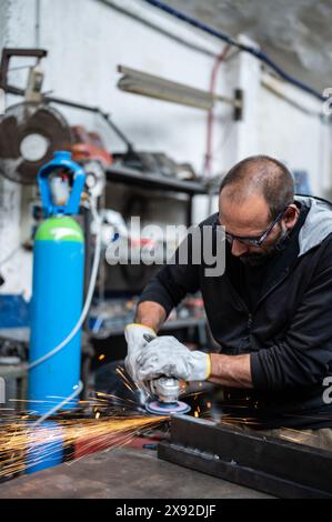 Using the flexible disc grinder on a metal bar: When the tool touches the surface, numerous orange sparks are projected. Vertical format. Concept of m Stock Photo