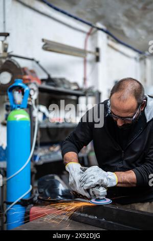 Using the flexible disc grinder on a metal bar: When the tool touches the surface, numerous orange sparks are projected. Vertical format. Concept of m Stock Photo