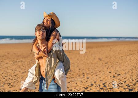 copyspace multicultural Latina woman smiles affectionately while being carried on her boyfriend's shoulders at the beach on a sunny summer day. Their Stock Photo