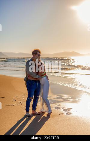 Hispanic couple embraces affectionately on the shoreline of the beach, silhouetted against the setting sun during a summer evening. Their loving embra Stock Photo