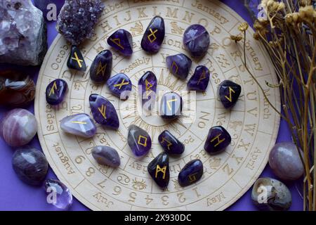 Amethyst crystals, Scandinavian runes and dry herbs on a purple background with a board with symbols of the zodiac signs. Predictions, witchcraft, spi Stock Photo