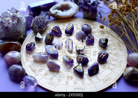 Amethyst crystals, Scandinavian runes and dry herbs on a purple background with a board with symbols of the zodiac signs. Predictions, witchcraft, spi Stock Photo