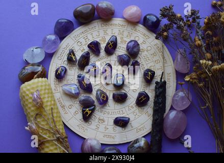 Scandinavian runes from amethyst and dry herbs on a purple background with a board with symbols of the zodiac signs. Predictions, witchcraft, spiritua Stock Photo