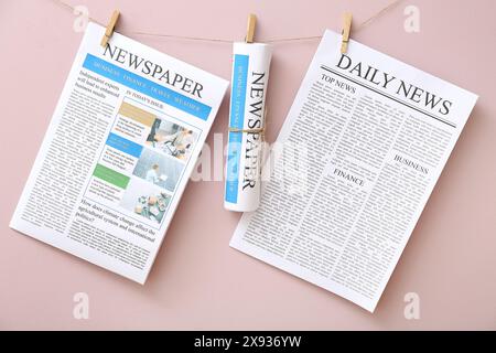 Different newspapers hanging on rope against pink background Stock Photo