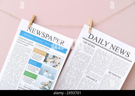 Different newspapers hanging on rope against pink background Stock Photo