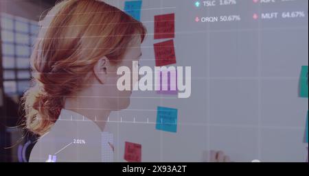 Caucasian woman in her early thirties looking at colorful sticky notes on whiteboard Stock Photo