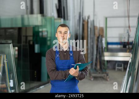 Technician inspecting glass panels and writing notes in workshop Stock Photo