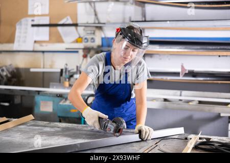 Workwoman cutting plastic profile with angle grinder in workshop Stock Photo