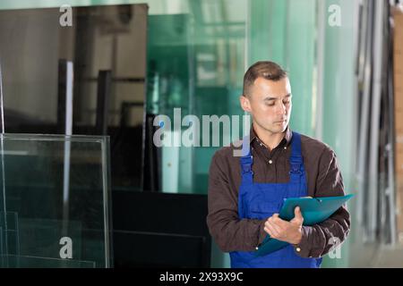 Worker inspecting glass panels and recording check results Stock Photo