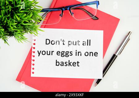 Don't put all your eggs in one basket text written on a torn piece of paper lying on a notebook Stock Photo