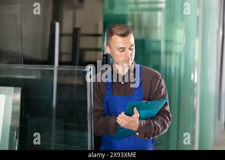 Focused technician inspecting and documenting glass panels in workshop Stock Photo