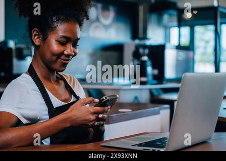 Portrait of cafe owner a concentrated black woman in apron using smartphone in her shop. Multi Stock Photo