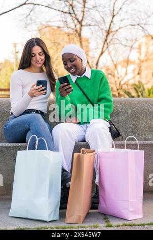 female friends using mobile phone sitting at park Stock Photo