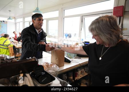 Prime Minister Rishi Sunak shakes hands with a cafe worker as he picks up breakfast for the media in Cornwall, while on the General Election campaign trail. Picture date: Wednesday May 29, 2024. Stock Photo