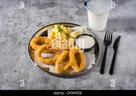 Fried calamari with potato salad next to it on stone table Stock Photo