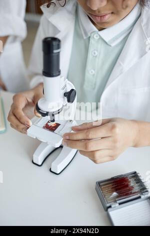 Vertical high angle view shot of middle school student sitting at desk using microscope during Chemistry or Biology lesson Stock Photo