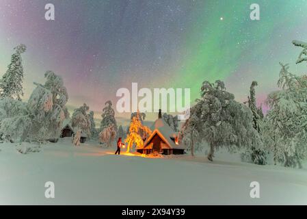 Hiker with lantern beside a mountain hut under Northern Lights (Aurora Borealis), Pallas-Yllastunturi National Park, Muonio, Finnish Lapland, Finland Stock Photo
